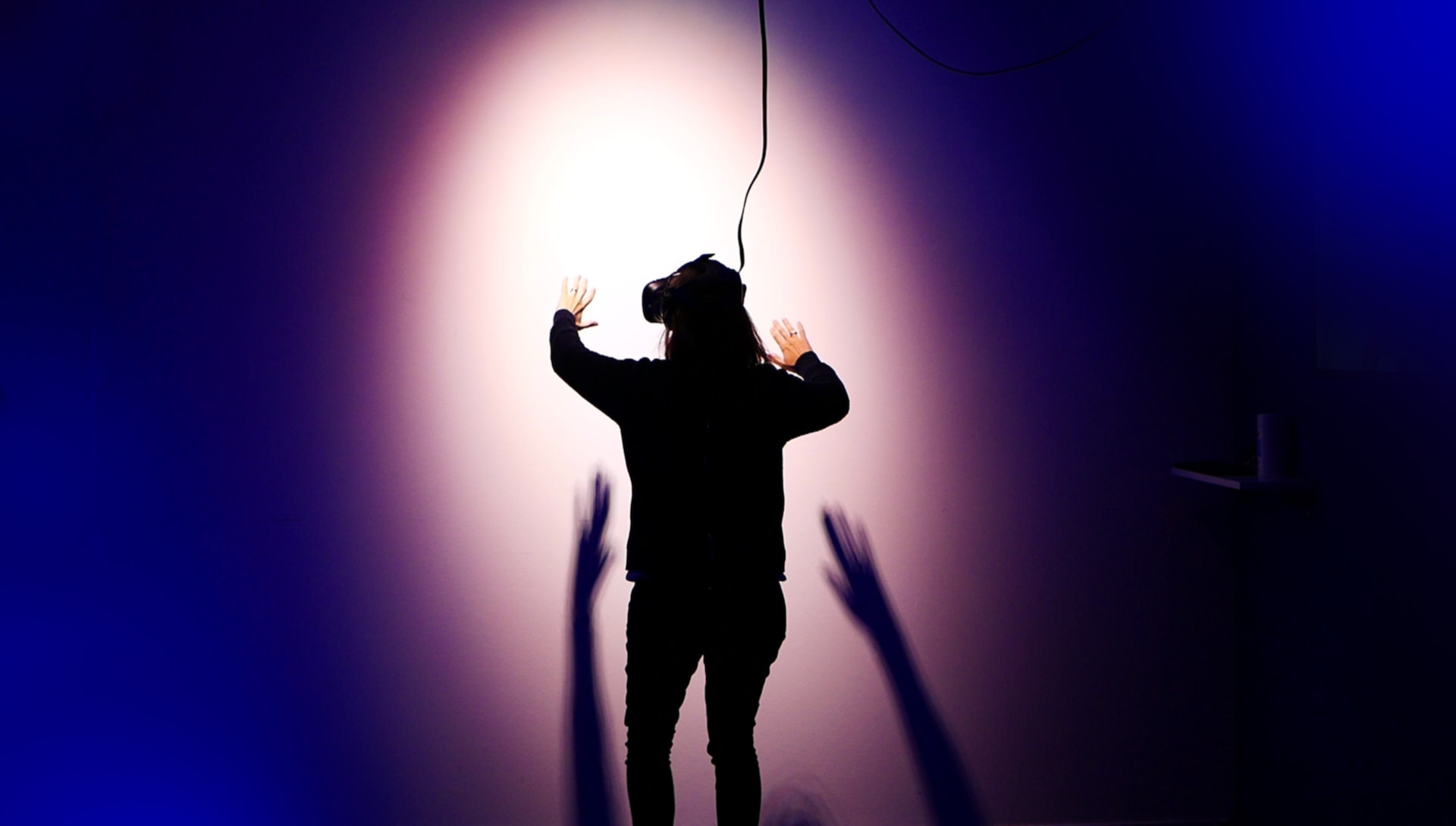 Fully immersed woman with a wired head-mounted device on her head using hand tracking in dark room with a spotlight on her.